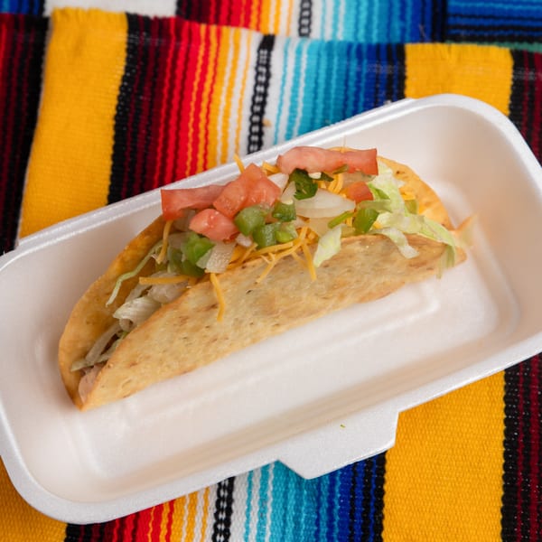 A Pepe's Mexican Café crispy taco with lettuce, cheese, tomatoes, and onions in a white container.