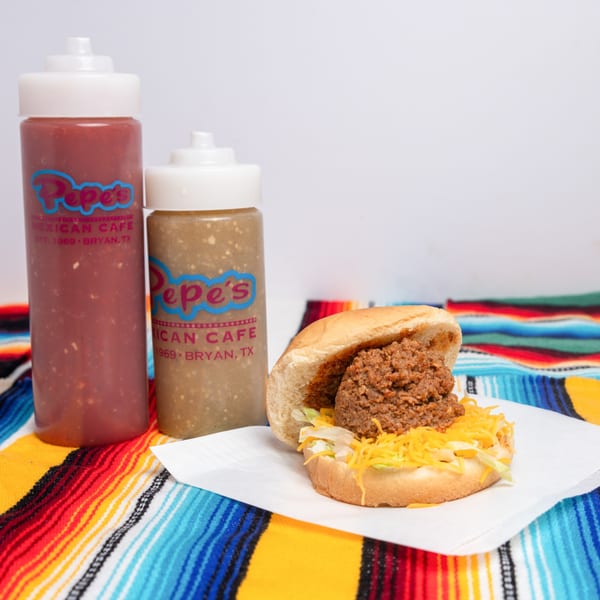 Pepe's Mexican Cafe bun with ground beef, cheese, and lettuce, alongside two squeeze bottles of salsa.