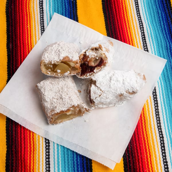 Three churros, two filled with apple and one with cherry, dusted with powdered sugar on a colorful striped blanket.