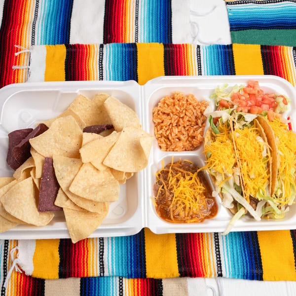 Pepe's Mexican Café takeout container with tacos, rice, beans, and chips on a colorful striped blanket.