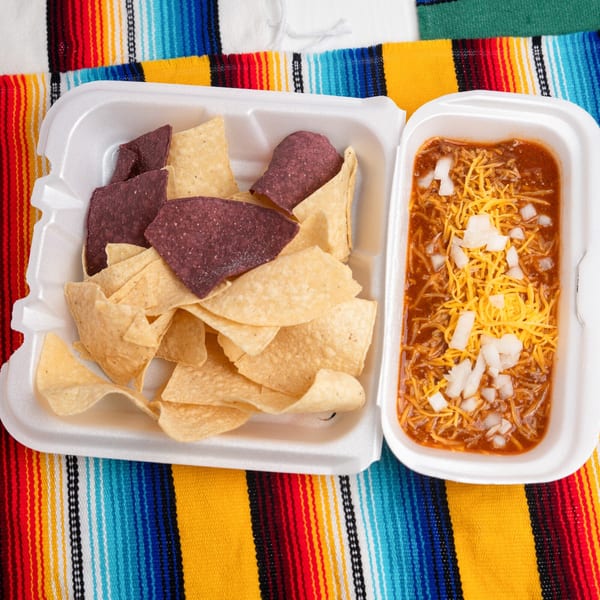 Pepe's Mexican Café chili with cheese and onions, alongside tortilla chips, in a takeout container.