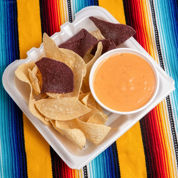 Pepe's Mexican Café chips and queso in a white to-go container on a colorful striped blanket.